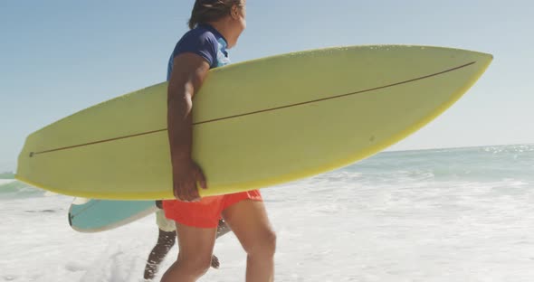 Senior african american couple running with surfboard on sunny beach