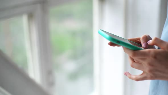 Close Up of Hands of Unrecognizable Young Woman Using Cell Phone Near Window.