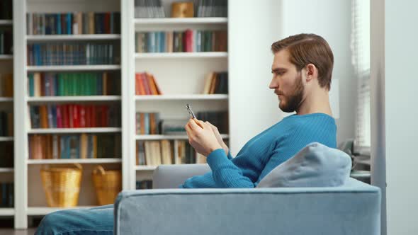 Concentrated man looks at bank card in hand and enters digits to smartphone