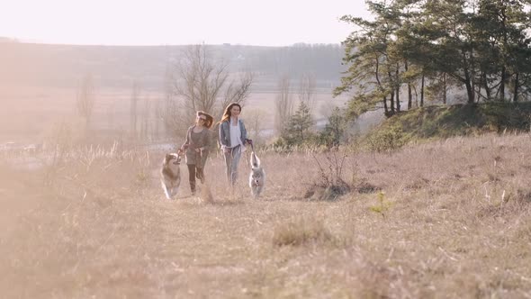 Two Young Pretty Women Are Walking with Fluffy Cute Dog in the Field