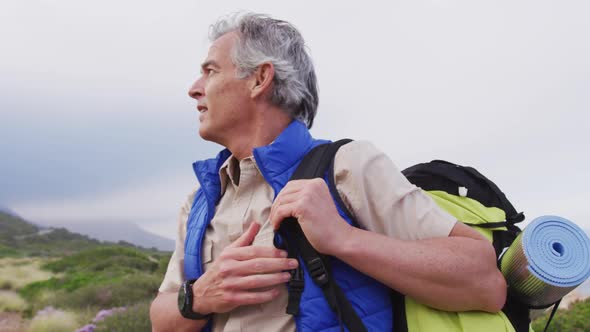 Senior hiker man with backpack standing and looking around while trekking in the mountains.