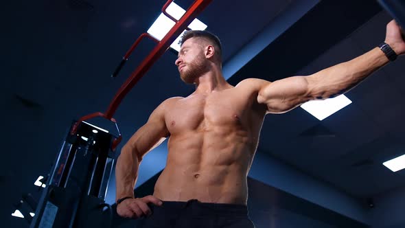 Muscular man over big gym background. Male with perfect nacked torso. Slow motion. View from below.