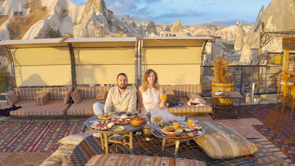 Happy couple on rooftop of an cave house enjoying brackfast and of Goreme city panorama Cappadocia