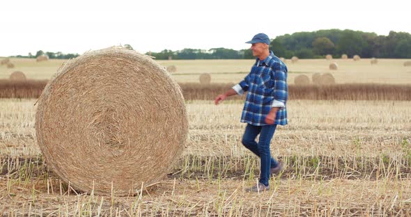 Smiling Farmer Rolling Hay Bale and Gesturing in Farm