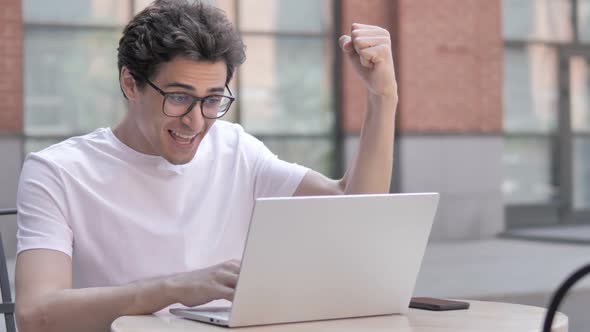 Young Man Celebrating Success on Laptop Sitting Outdoor