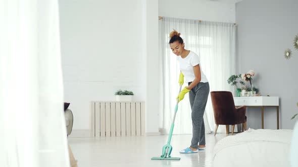 Pretty African American Girl Is Mopping Floor at Home with Flat Plastic Mop Wearing Gloves and Wear
