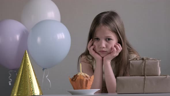 Upset Little Girl Looking Sad Because Celebrating Birthday Alone Over Background of Gifts and