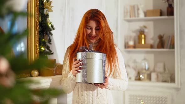 Beautiful Woman Smiles at Camera with New Year Gift in Hands Near Christmas Tree