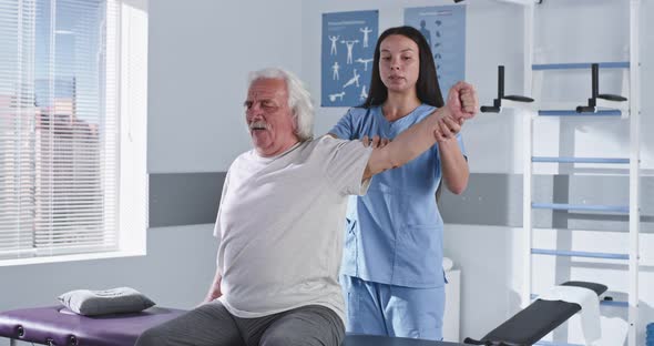 Rehabilitation Therapist Stretching Arm of Elderly Man
