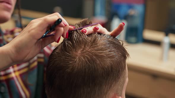 Barbershop, close-up: woman barber cuts men's hair with scissors