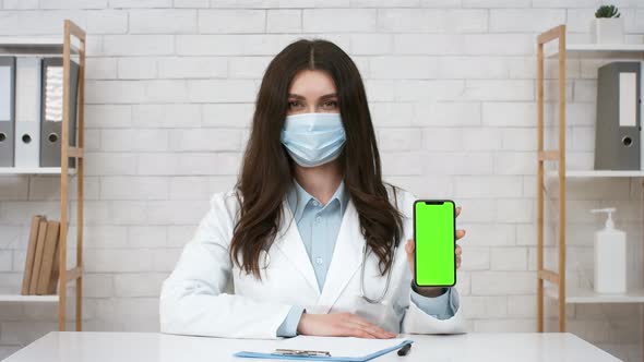 Female Doctor Showing Cellphone Screen Wearing Face Mask In Office