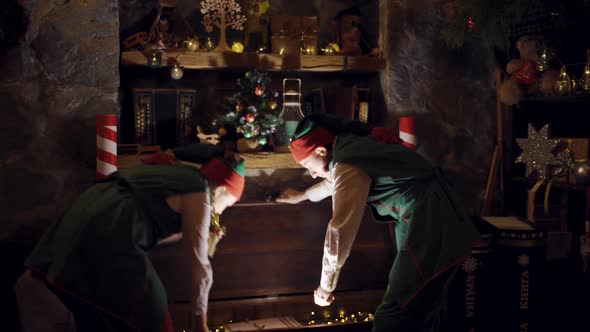 Curious elves in small decorated room opening the magic box. Two elves in fairy suits