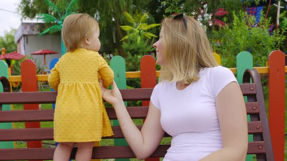 Caucasian young woman with a funny baby girl sitting on a bench.