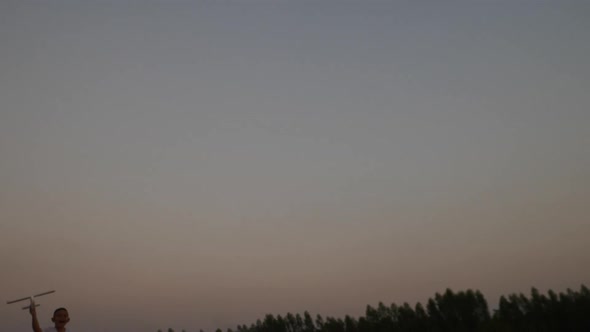 Boy playing wood airplane in the hands of running on a field at sunset