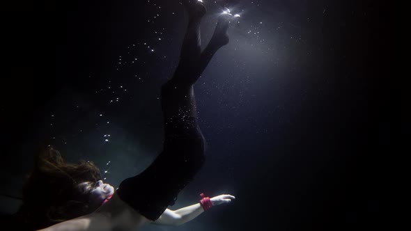 A Beautiful Darkhaired Woman in a Red Mask and Red Handcuffs Swims Deep Under the Water