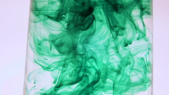 Green food coloring swirling in a glass of water .