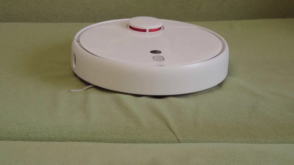 Hand turns on the robot vacuum cleaner. A smart vacuum cleaner cleans the bed. Smart home