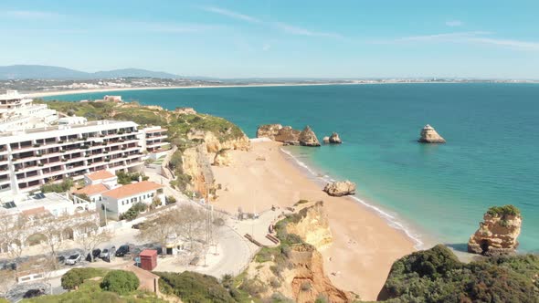 View over green hill shrouding golden Dona Ana beach, Lagos, Algarve, Portugal