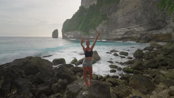 Cheering female tourist taking selfie on rocky shore in Nusa Penida secluded beach