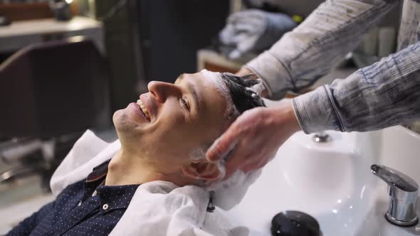 a Hairdresser Washes the Hair of a Brunette Man in a Barbershop