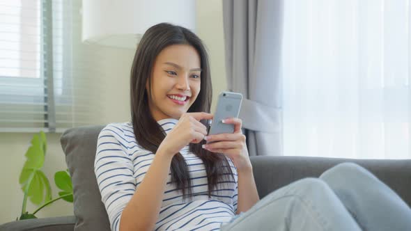 Asian young beautiful woman playing mobile game on smartphone at home.