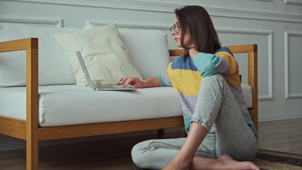 Young Woman Using Laptop Using Touchpad Sitting on the Floor Near the Sofa at Home Remote Work Work