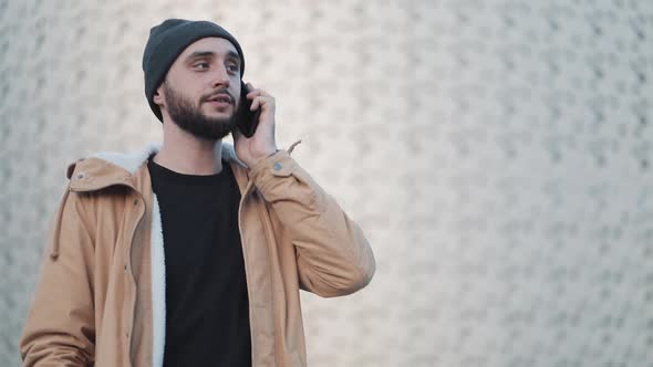 Happy Young Beard Man Calling on Mobile Phone Walking in the Street Near Shopping Mall. He Is