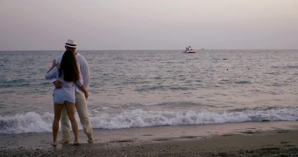 Adult Man and Woman Are Holding Hands and Running To Sea Water Line on Beach in Dusk