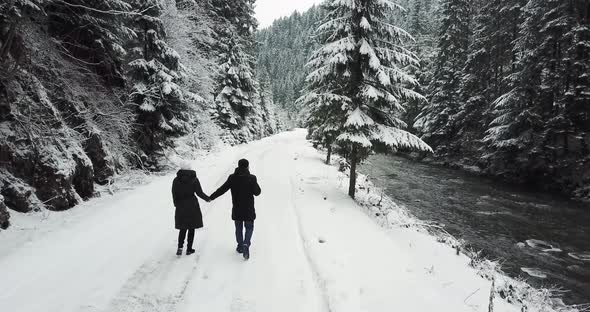 A Couple in Love Walks on a Snowy Road in the Middle of the Forest They Hold Hands