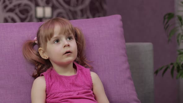 Little Child Sitting on Couch While Watching TV. Kid Girl Watch Television