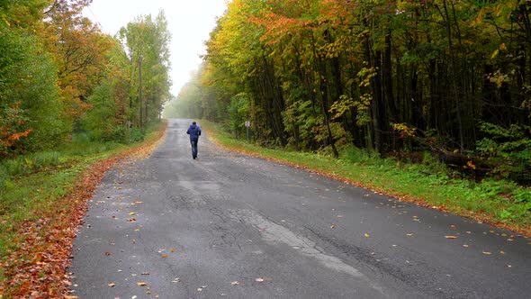 Man running on a small road surrounded by maple autumn maple leaf