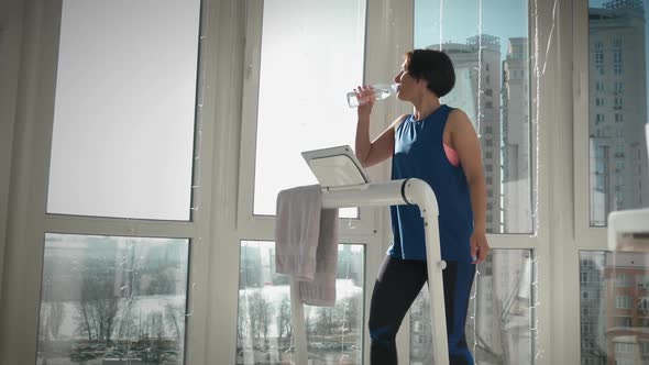 Young slim fit woman is drinking water to stay hydrated during fitness workout