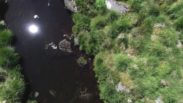 Birdseye close up aerial tracking forward of a rocky river following downstream surrounded by grassy