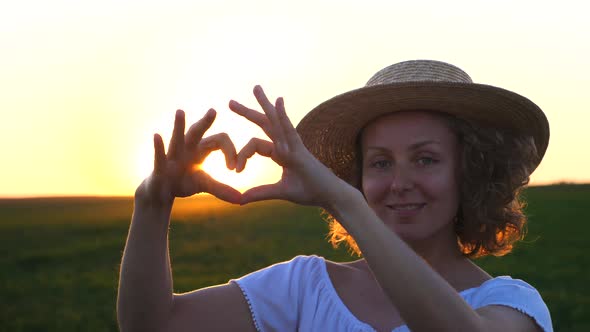 Girl Making A Heart-Shape With Her Hands In Field At Sunset