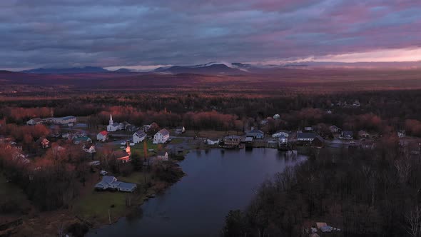 Aerial footage flying backwards away from small community on shore of lake at sunrise in late fall w