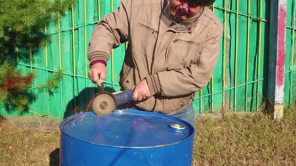 A Man with a Grinder is Cutting the Bottom Out of a Barrel