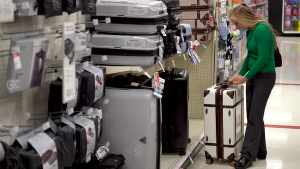 Wide shot of pretty mature woman looking at travel luggage in a store display.