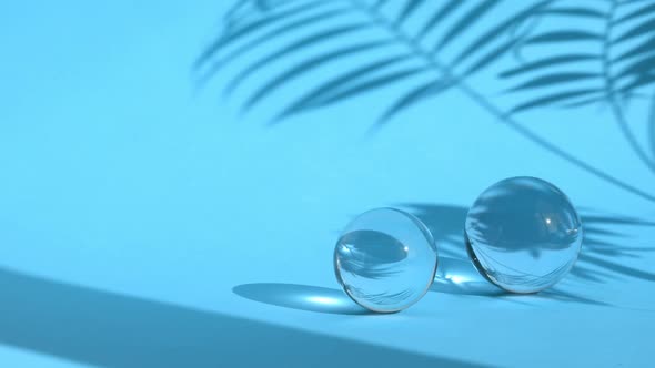 Astract Backdrop with Glass Spheres on Blue Color Background with Sun Reflections and Palm Leaf
