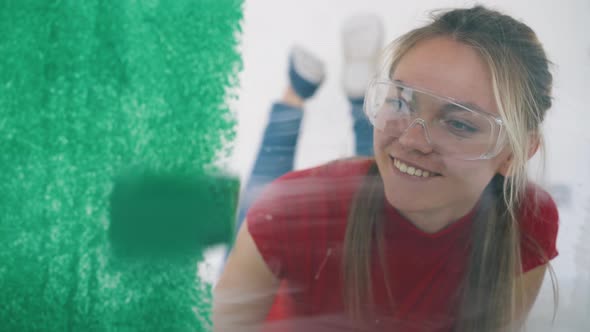 Girl in Goggles Paints Wall with Green Using Roller in Room