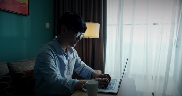 Young Attractive Asian Vietnam Man Busy Work Computer or Smart Tablet on Laptop at Home in Freelance