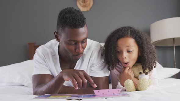 African american father reading a story to his daughter in bed