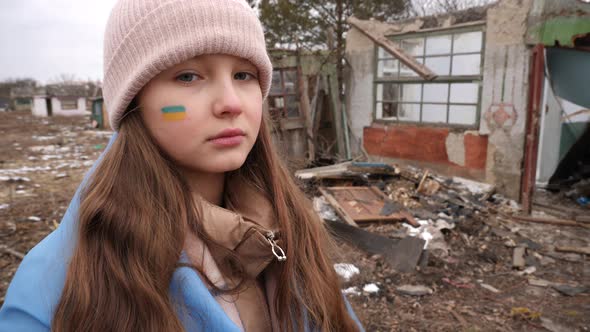 Portrait of a girl with a Ukrainian flag on her cheek against the background of destroyed houses. Wa