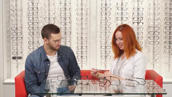 Beautiful Redhaired Woman Oculist Helps To Choose Glasses Man Client