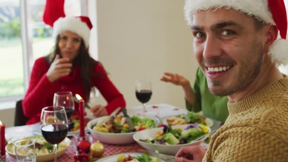 Happy caucasian man wearing santa hat looking at camera during christmas meal