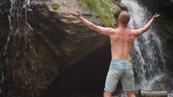 Man Tourist Raises Up Hands Enjoying Waterfall at Highland