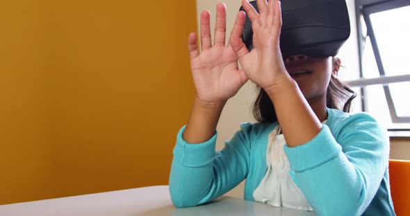 Schoolgirl using virtual reality glasses in classroom at school