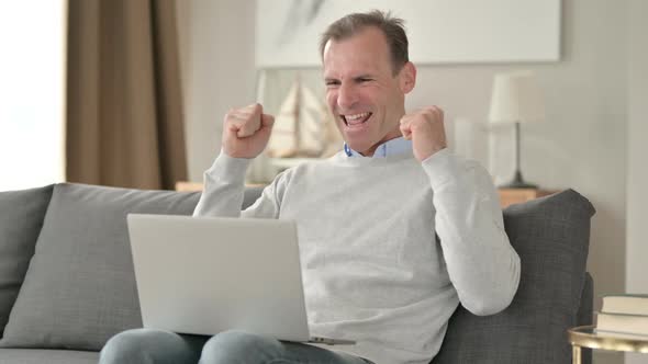 Surprised Middle Aged Businessman Celebrating Success on Laptop on Sofa