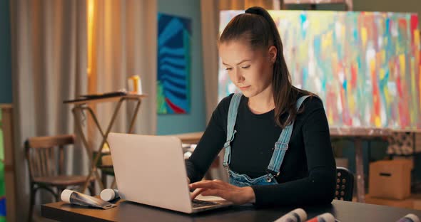 Beautiful Young Painter Relaxes in Living Room Painting Studio Sits at Desk in Front of