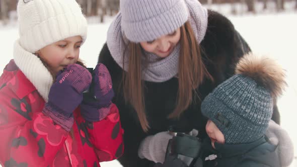 A Young Woman Drinking Hot Drinks with Her Children Outdoors