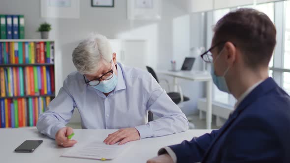 Senior Man in Medical Mask Sign Document in Lawyer Office